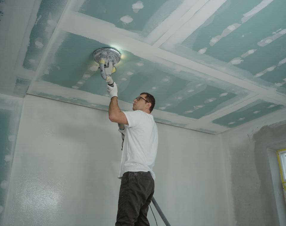 A man is working on the ceiling of his room.